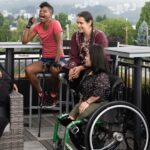 Five women sat around a table outside - one wheelchair user, one using a stick, one visually impaired and one with a proshthetic limb all of different nationalities