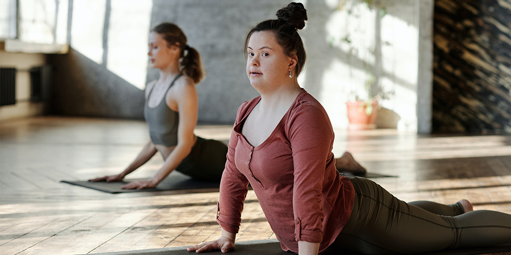 Two woman, one with Down's Syndrome, doing yoga on mats in a gym