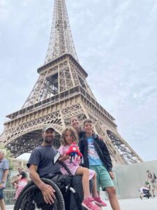 Rob in his wheelchair sits with his two children and wife at the base of the Eiffel Tour.