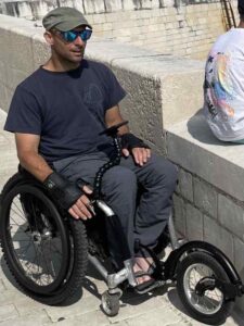 Rob is in his wheelchair with a freewheel attached. The Flexi Phone Holder is attached to his chair, holding in phone in place in front of him for navigating.
