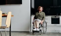 Woman using a wheelchair wheeling out from her open-plan kitchen into her dining room
