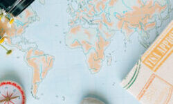 A world map laid out on a table with a camera in the top right corner and a compass and passport cover