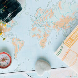 A world map laid out on a table with a camera in the top right corner and a compass and passport cover