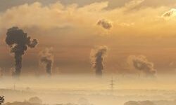 Smoke from factories and electricity pylons against a sunset
