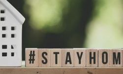 Stay home words spelt out on wooden letter blocks next to a white china house