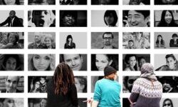Three people sat on a bench in front of a wall of black and white portraits of people