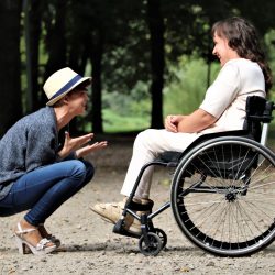 Two friends smiling next to each other, one in a wheelchair and one squatting down.