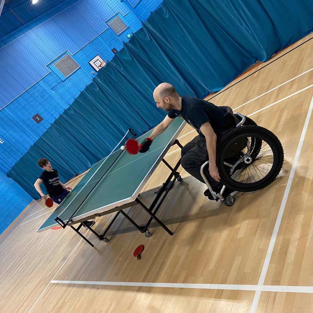 Rob plays table tennis against his nephew, holding the racket with an angled aid.