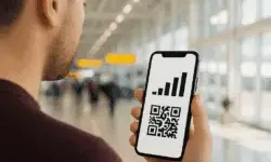 A person at an airport holds a smartphone displaying a signal strength icon above a QR code, showing eSIM activation.