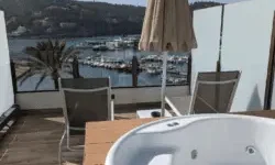 Empty hot tub on a balcony overlooking a marina with yachts, hills, and palm trees in the background.