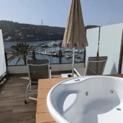 Empty hot tub on a balcony overlooking a marina with yachts, hills, and palm trees in the background.