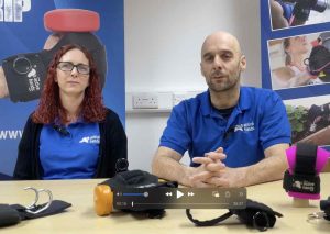 Image shows rob and clare looking to camera. They are sat at a desk with a variety of our gripping aids displayed. They are both wearing Active Hands blue t-shirts.