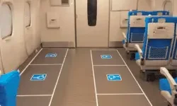 Wheelchair spaces with accessibility symbols marked on the floor inside a Shinkansen train car. Blue passenger seats line the right side.