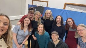 selfie of a group of smiling adults in front of a blue background. This is the Active Hands staff team.