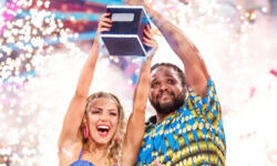 Hamza Yassin and Jowita Przystal lifting the Strictly glitterball. They are wearing brightly coloured blue and yellow outfits that they performed in for their Couple's Choice, an Afrobeats-inspired dance. There are fireworks behind them.