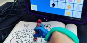 function hand used for colouring, with EazyHold strap over hand to help with grip, with communication aid directing colours
