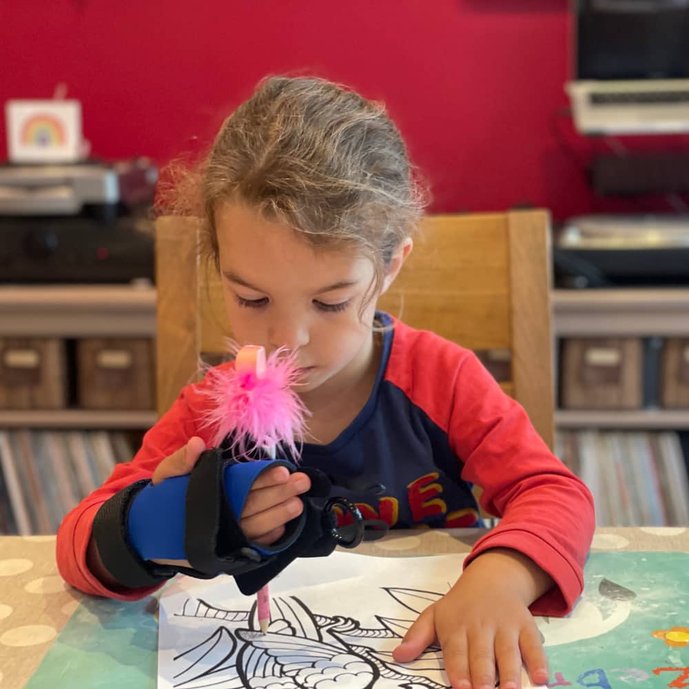 A child uses the mini small item aid to hold a pencil for drawing.
